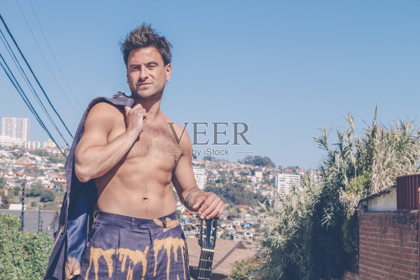 在Viña del Mar，瓦尔帕莱索，智利，一名肌肉发达的时尚男子，穿着蓝色西装外套，手拿原声吉他站在街道中央。时尚的年轻人。照片摄影图片