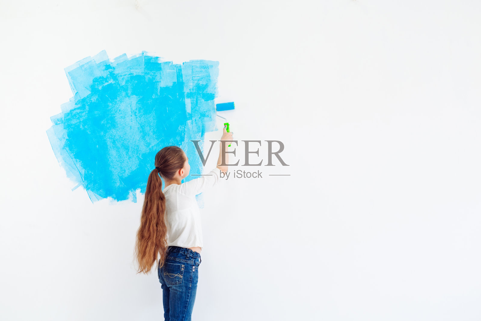 在公寓里修理。快乐的小女孩用蓝色的油漆涂墙，照片摄影图片