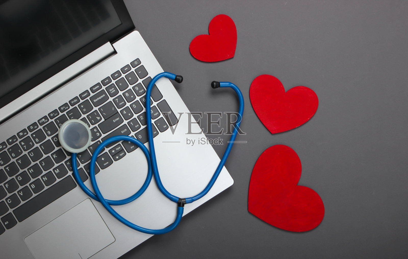 笔记本电脑和灰色背景上有心脏的听诊器。俯视图照片摄影图片