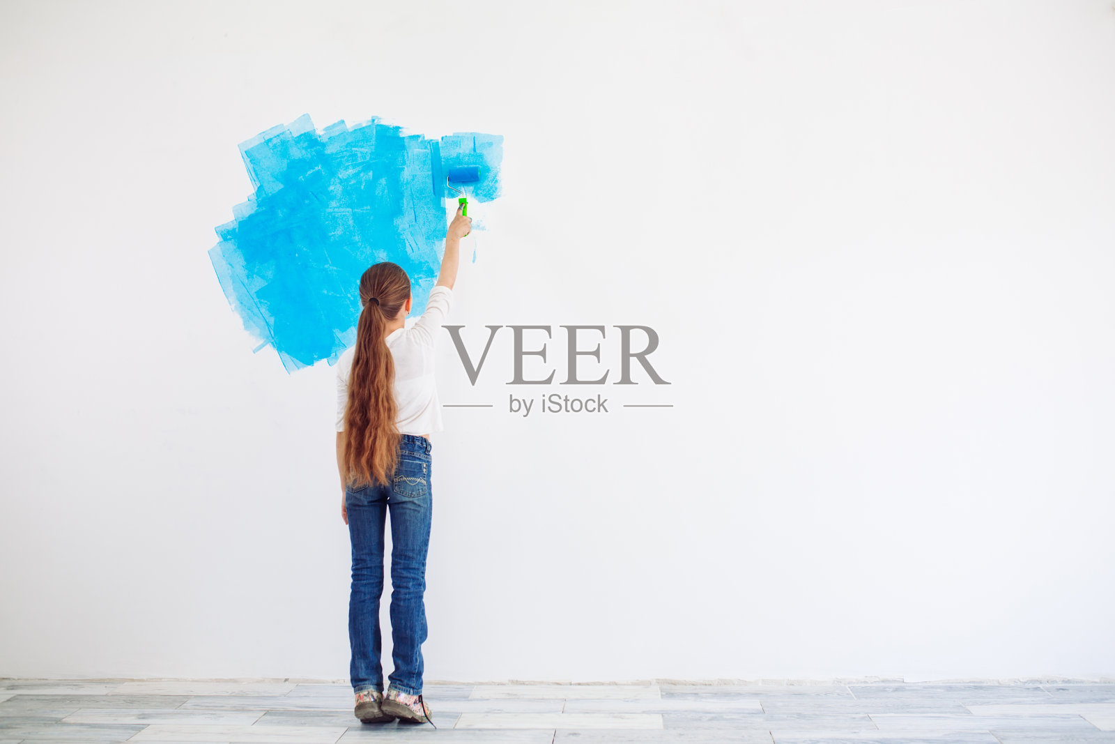 在公寓里修理。快乐的小女孩用蓝色的油漆涂墙，照片摄影图片