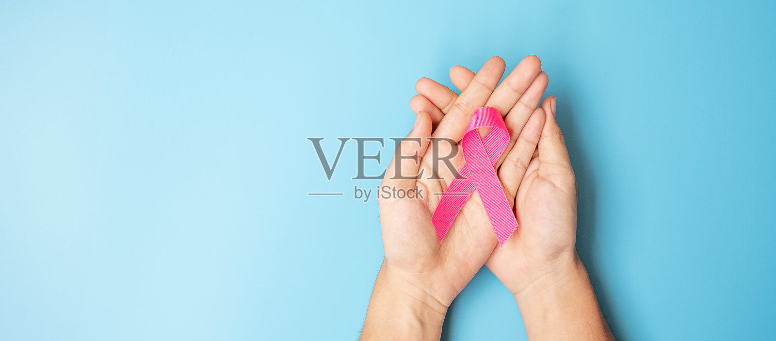 十月乳腺癌宣传月，成年妇女手拿粉红丝带在蓝色背景下支持人们生活和疾病。国际妇女、母亲和世界癌症日的概念照片摄影图片