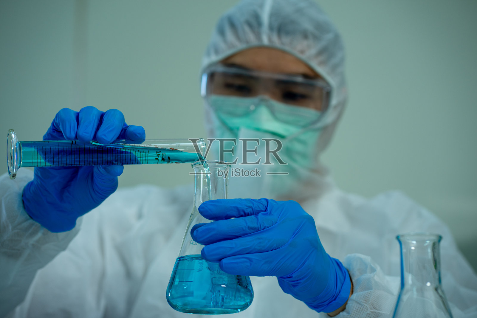 穿着白色防护服，戴着眼镜和面罩的亚洲医学科学家在临床实验室用显微镜诊断病毒照片摄影图片