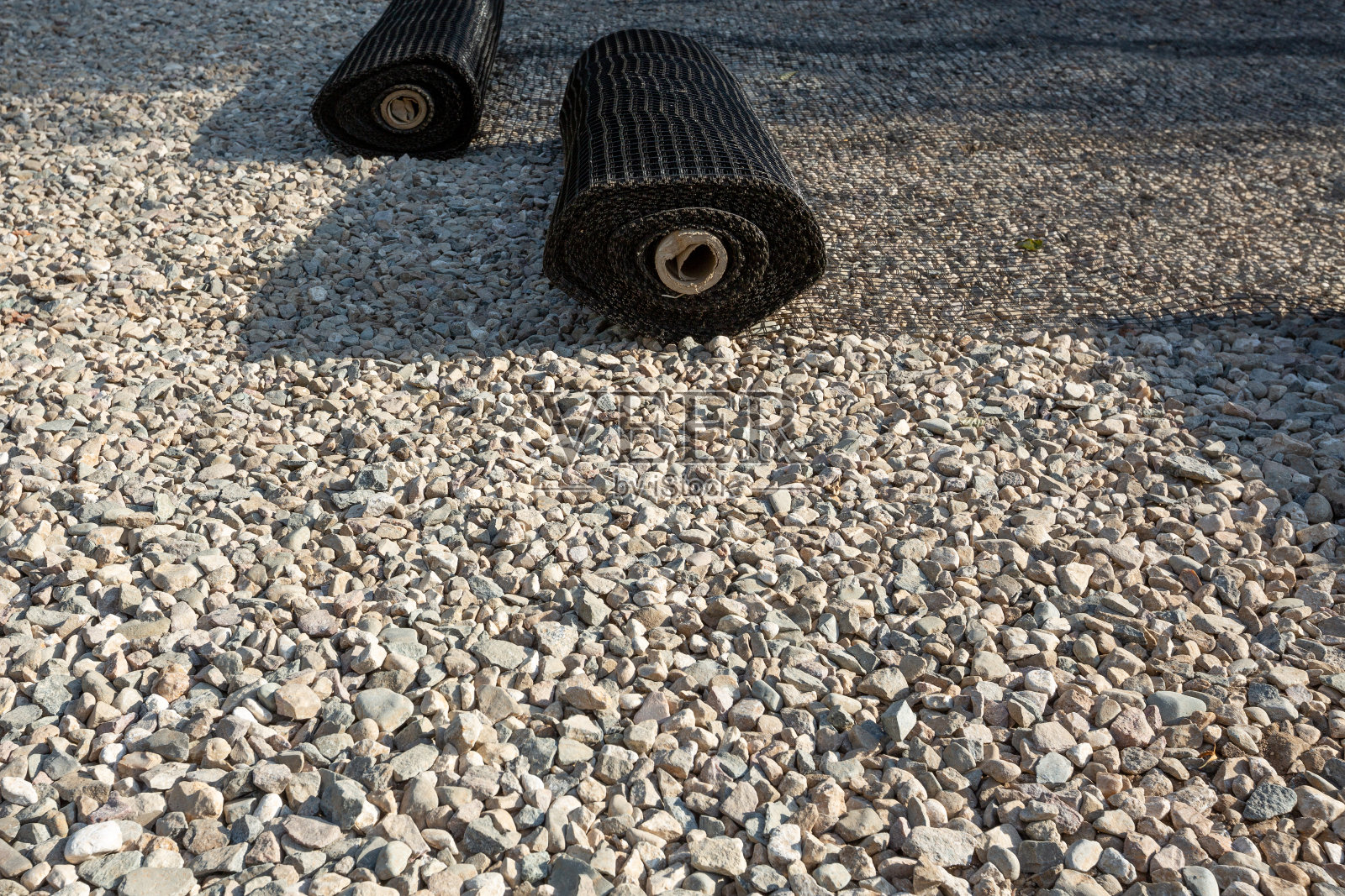 一卷卷合成土工格栅在砂砾上展开。照片摄影图片