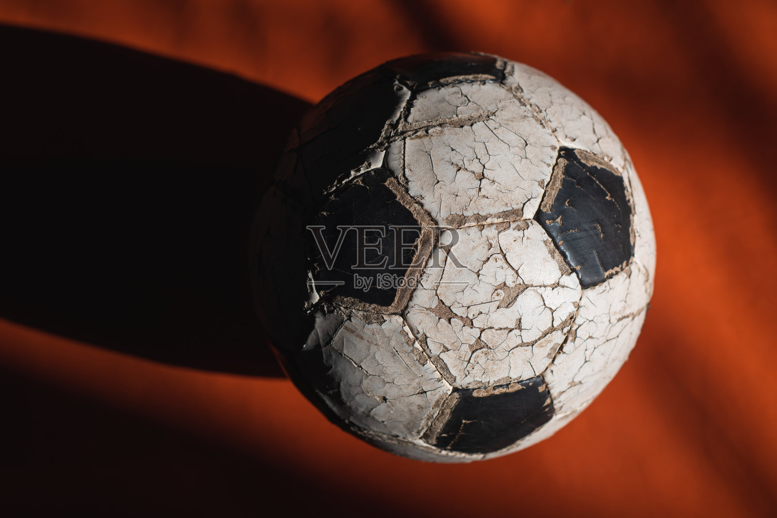 在一束光的黑暗背景上，一个破裂的旧足球。照片摄影图片