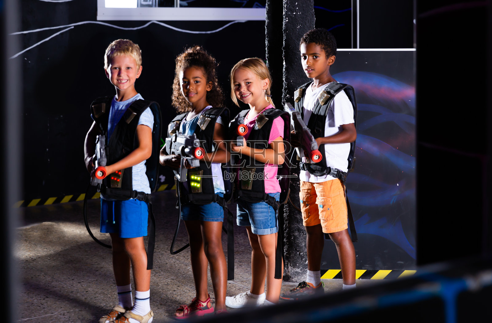 积极微笑的青少年与激光枪在黑暗的激光擂台上玩的集体肖像照片摄影图片