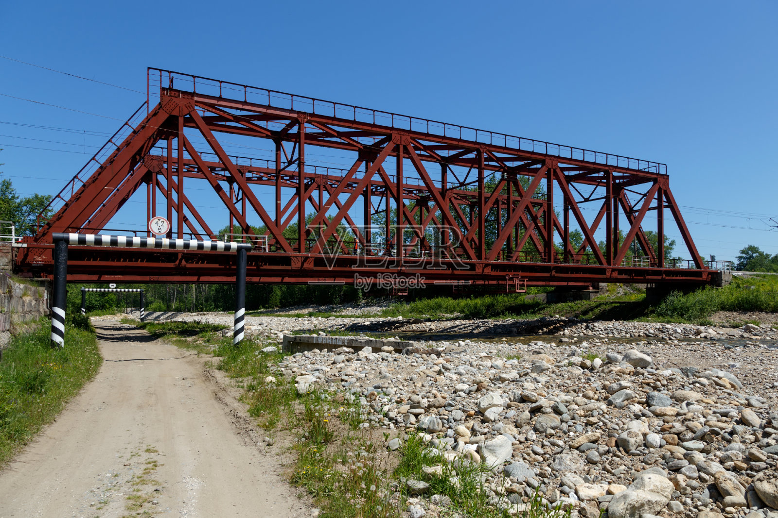 俄罗斯乌图利克- 2020年6月15日:红色金属铁路桥横跨一条小山河，下面是一条农村公路照片摄影图片