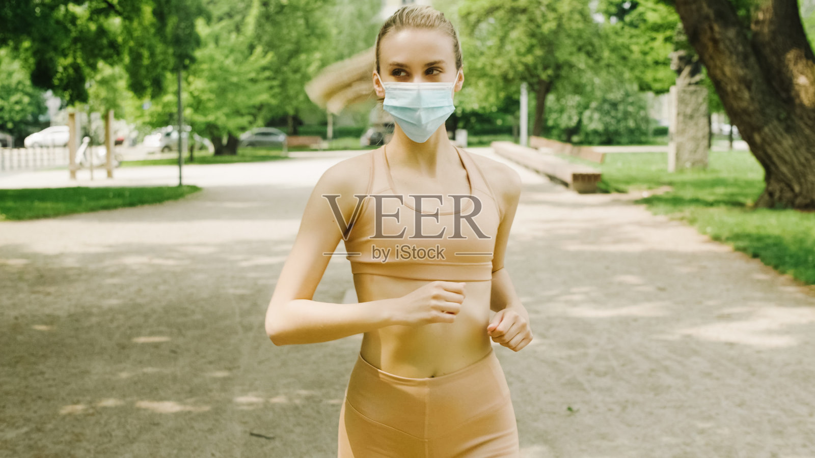 年轻活跃的女人戴着面具在城市公园慢跑。照片摄影图片