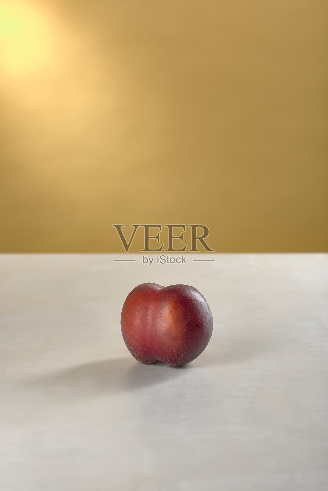 黄色背景的白色大理石桌上放着一颗油桃照片摄影图片