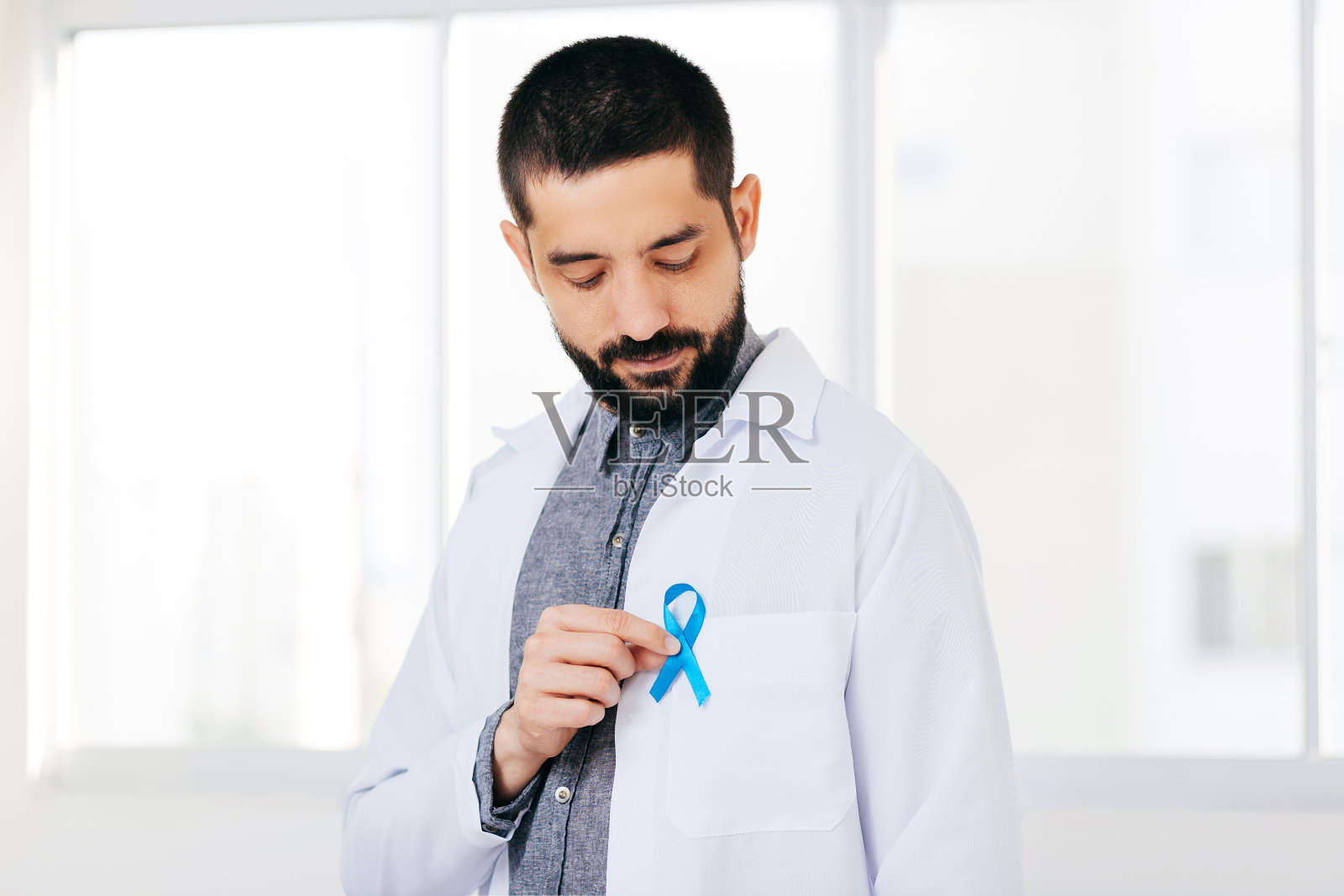 前列腺癌意识。一名手持浅蓝丝带的医生帮助人们生活和疾病。男性保健和世界癌症日的概念照片摄影图片