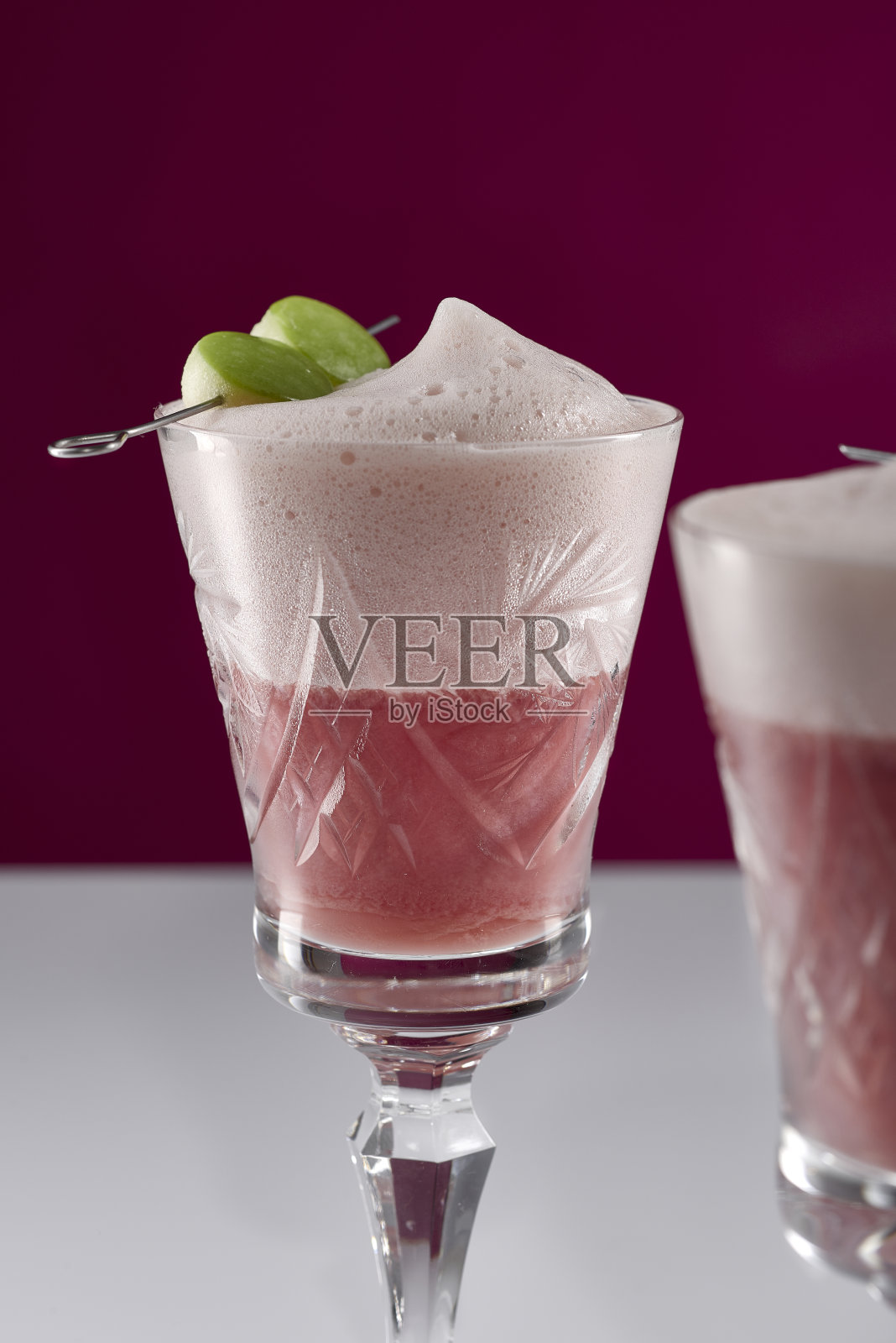 两个粉红色的饮料在复古水晶玻璃杯与苹果串在白色反光表面与粉色背景的特写照片摄影图片