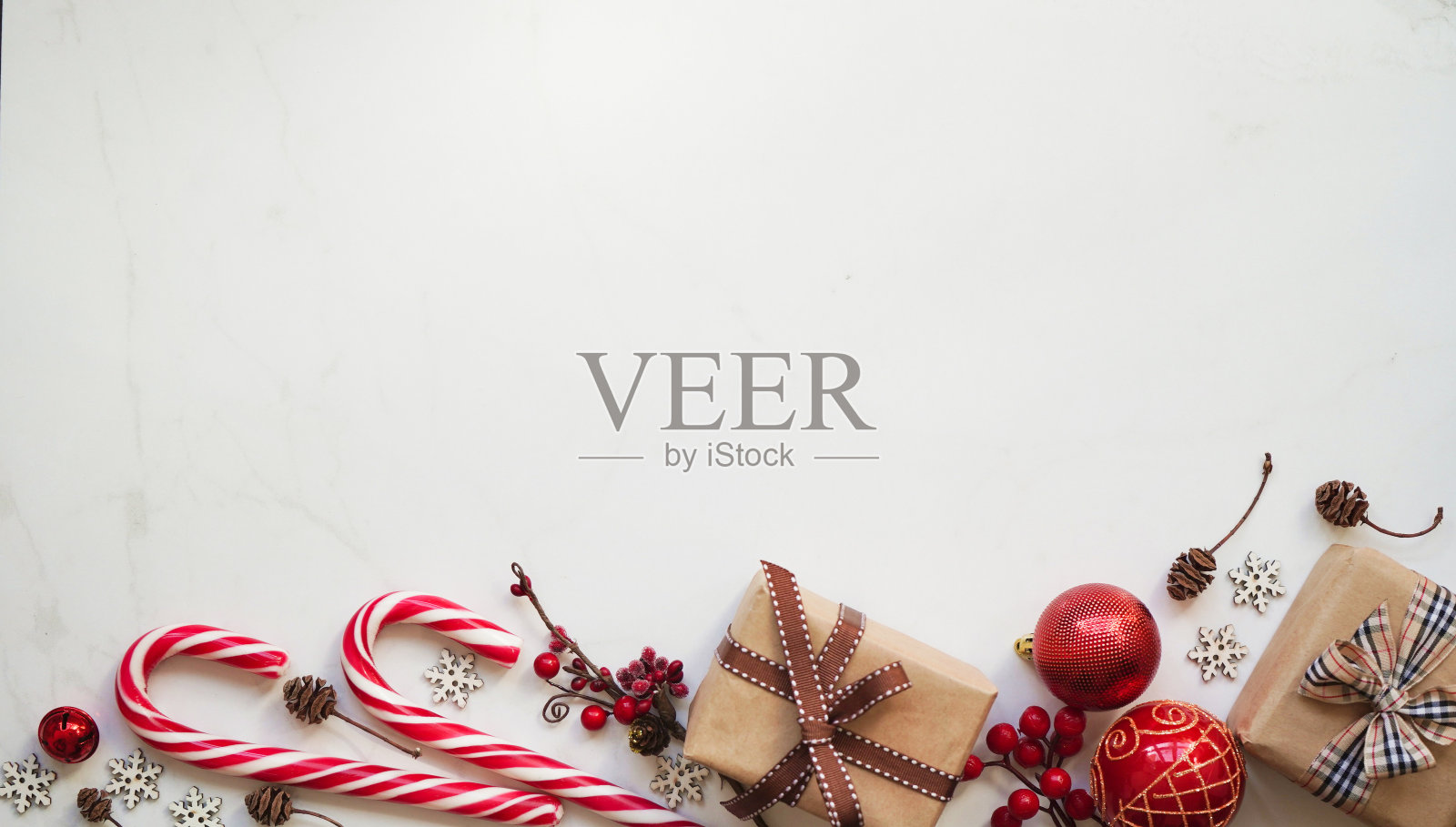 用牛皮纸包装的礼盒，用丝带绑着，圣诞红色玩具和棒棒糖，松果和雪花，白色背景上的红色浆果，俯视图，拷贝空间。圣诞节和新年的概念照片摄影图片