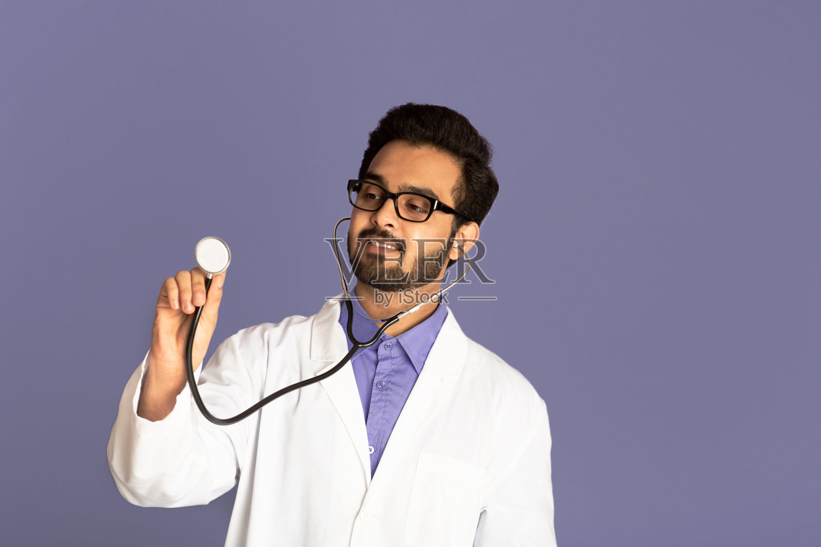 年轻的印度医生在实验室大衣使用听诊器在丁香背景，自由空间照片摄影图片