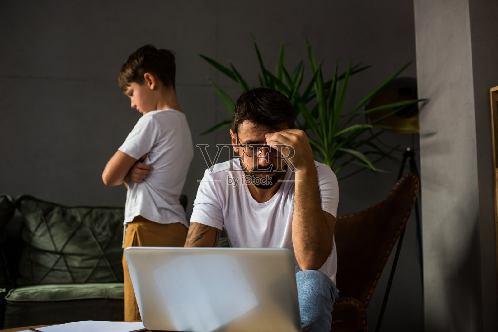 父亲和儿子一起在客厅里，父亲在网上做他的工作，他的儿子很生气照片摄影图片