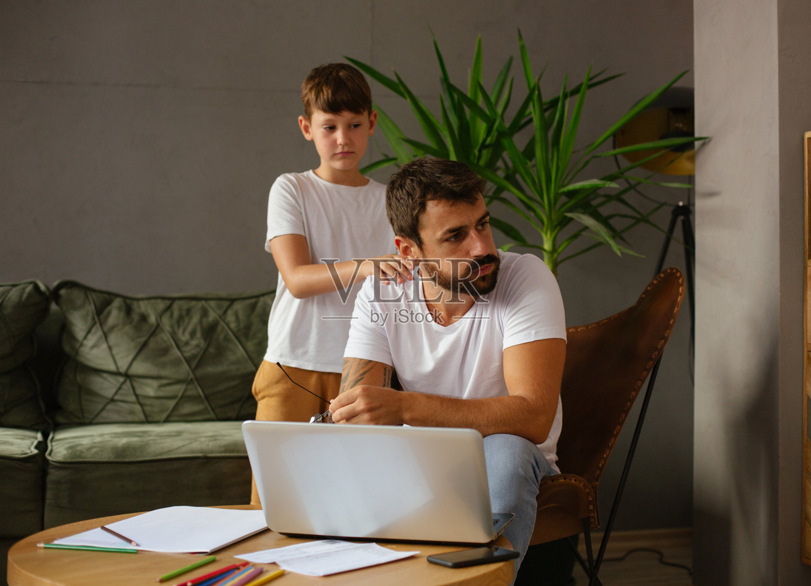 父亲和儿子一起在客厅里，父亲不得不上网工作，儿子很生气，不耐烦地问他什么时候才能完成工作照片摄影图片