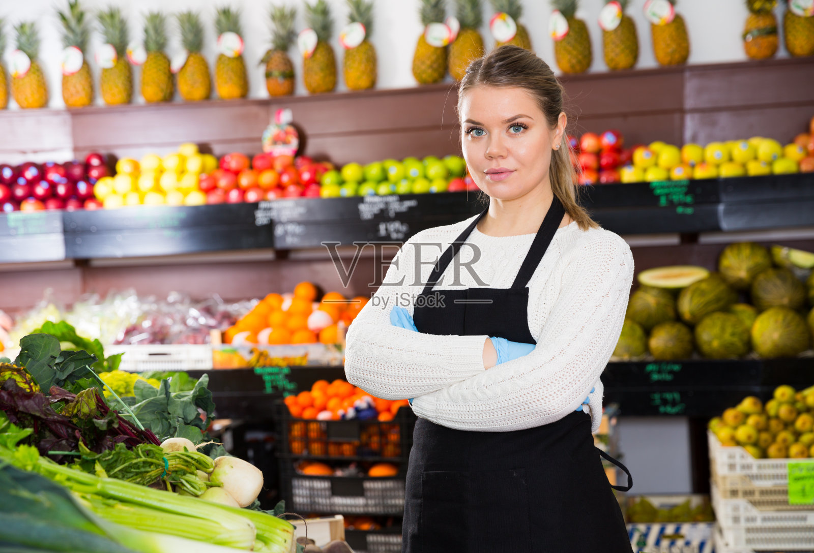 年轻的女售货员戴着手套，正在加工新鲜的绿叶蔬菜和莴苣照片摄影图片