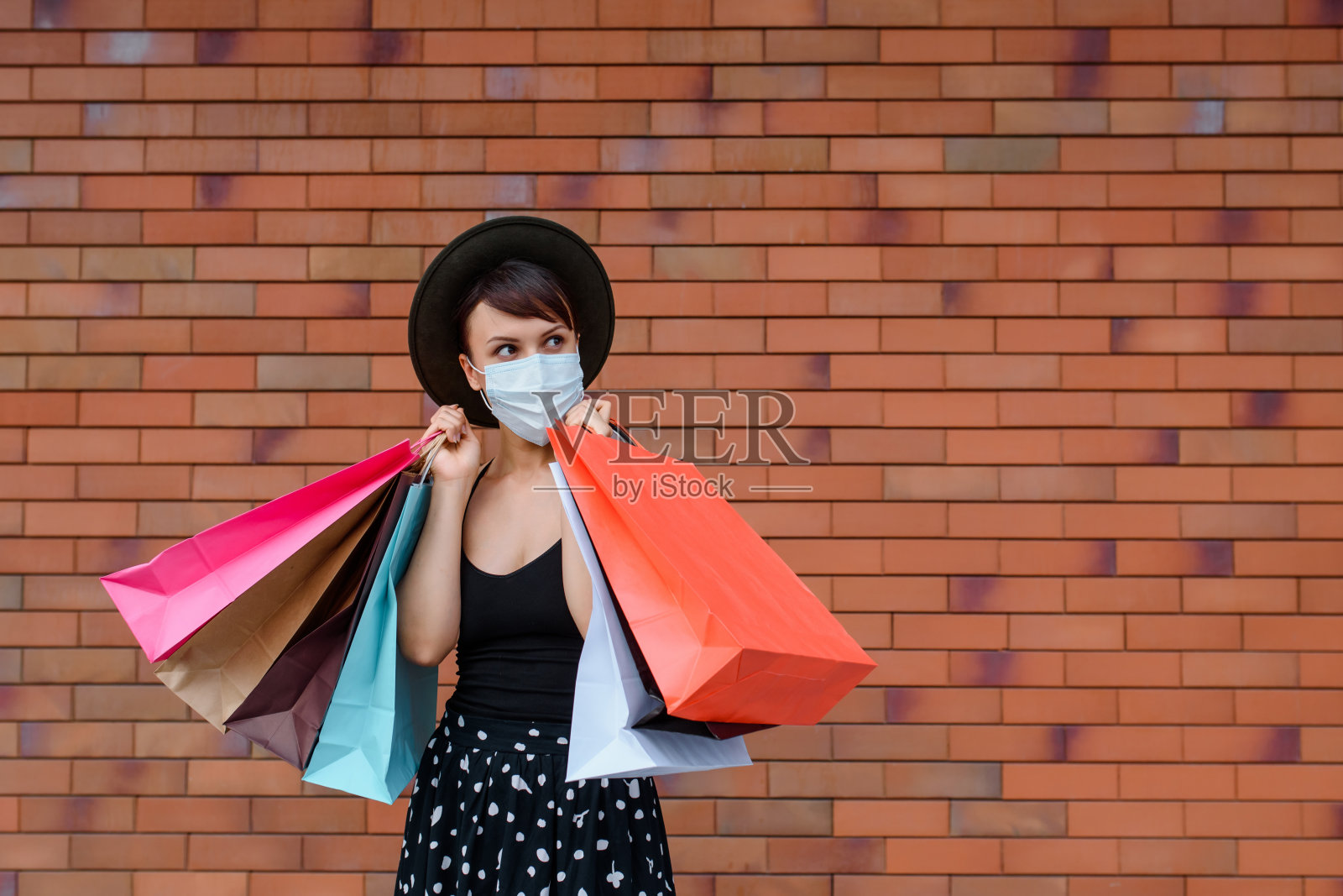 一名年轻女子戴着保护面罩，在一个美好的购物日之后，拿着许多五颜六色的购物袋。照片摄影图片
