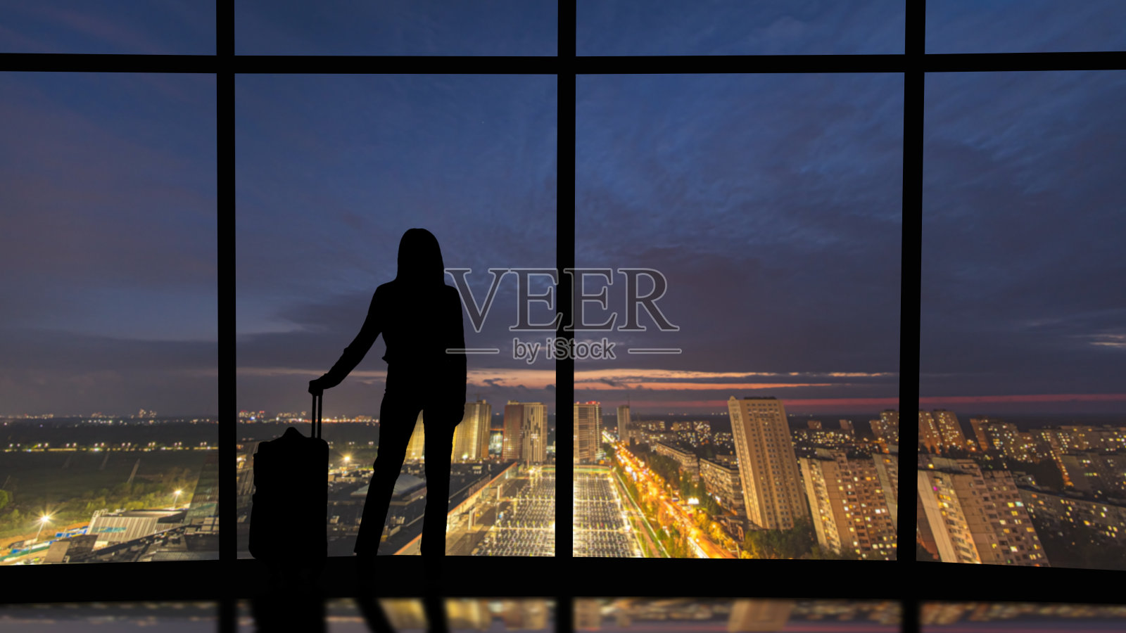 那个提箱子的女人站在商务办公楼靠窗户的地方照片摄影图片