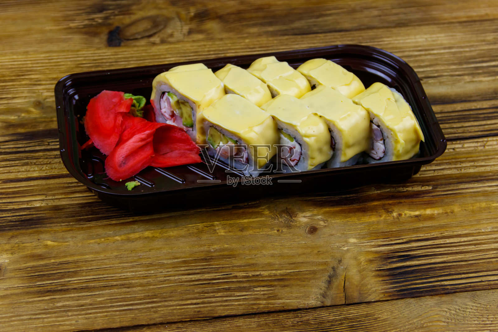 寿司芝士卷在塑料盒里放在木桌上。装在塑料容器内的寿司供外卖或运送照片摄影图片