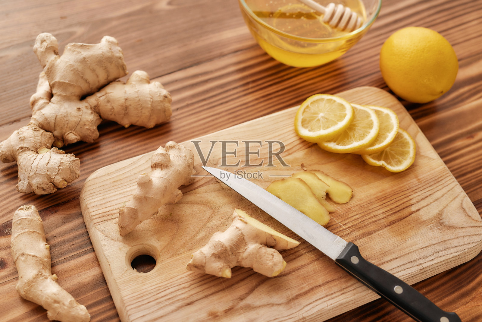 准备感冒治疗饮料，板、刀、鲜姜、柠檬、蜂蜜合在碗里用长勺放在木桌上照片摄影图片