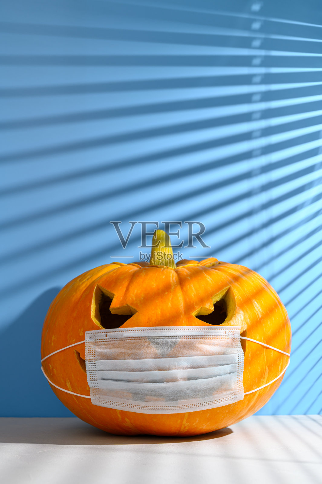 新标准的概念。发光的万圣节南瓜在一个保护性的医疗面具在一个柔和的蓝色背景。照片摄影图片