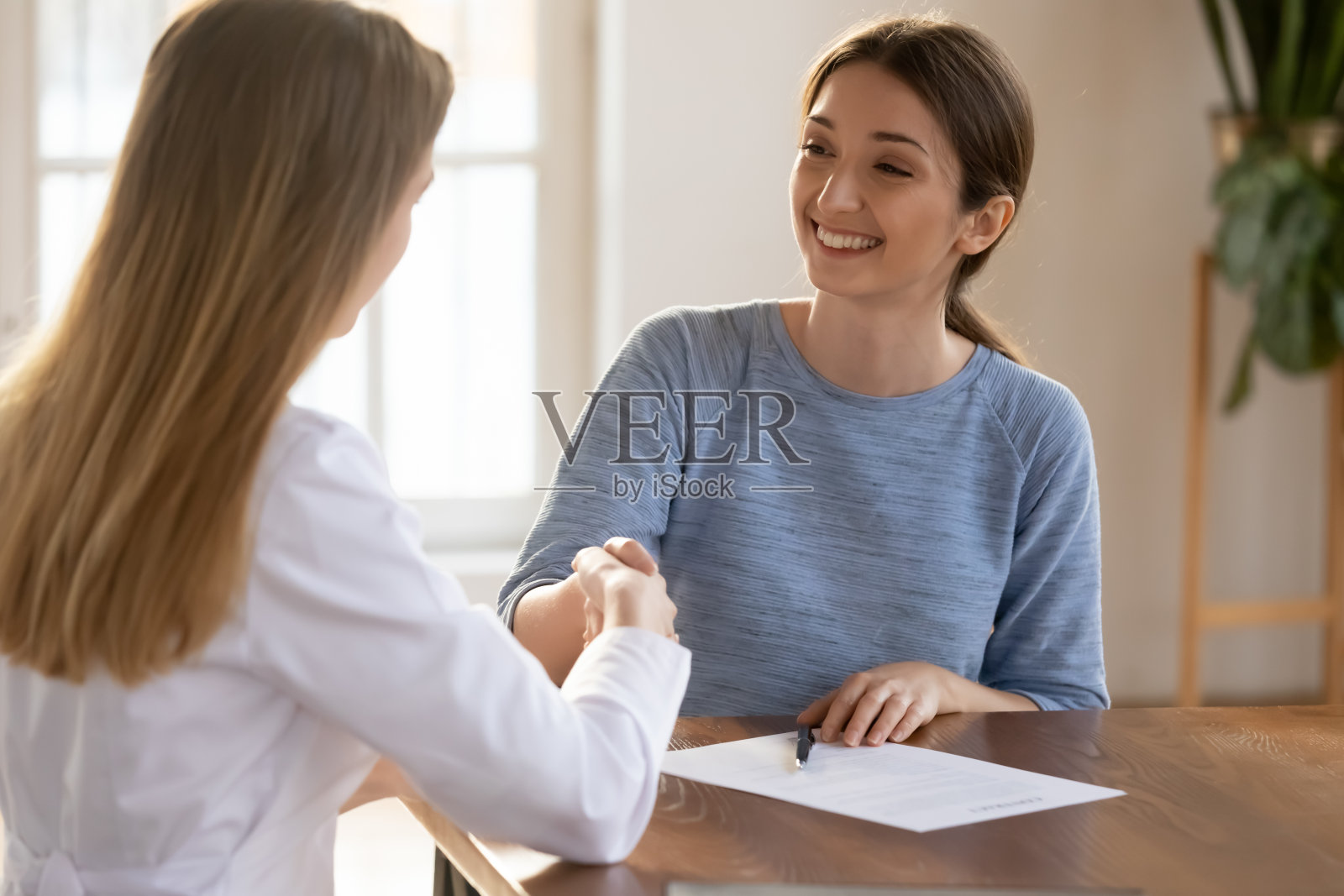年轻女子微笑着与医生握手，签订医疗保险合同照片摄影图片