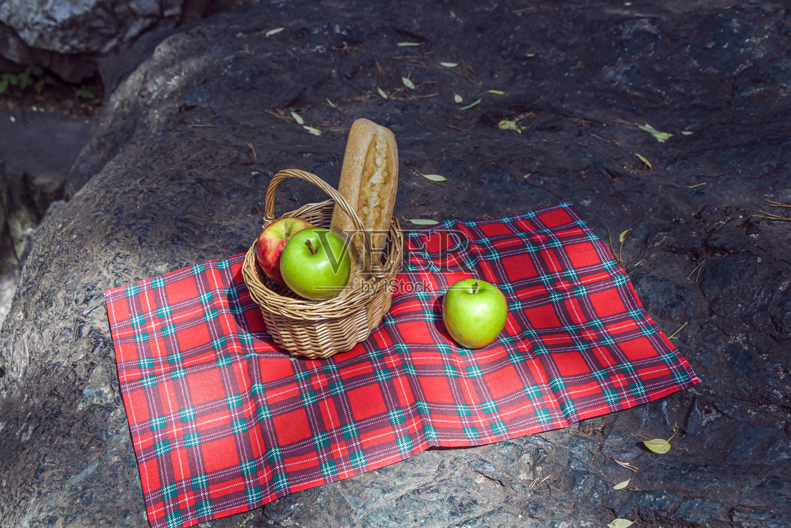 野餐篮子，长棍面包和水果，格子布上的石头。浪漫的静物秋夏郊游，午餐在自然照片摄影图片