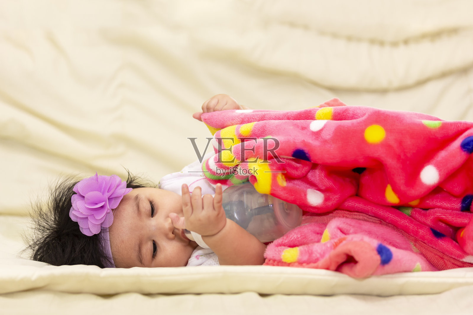 肖像亚洲可爱的婴儿在一个毯子吮吸奶瓶后，高兴地醒来在床上的房间照片摄影图片