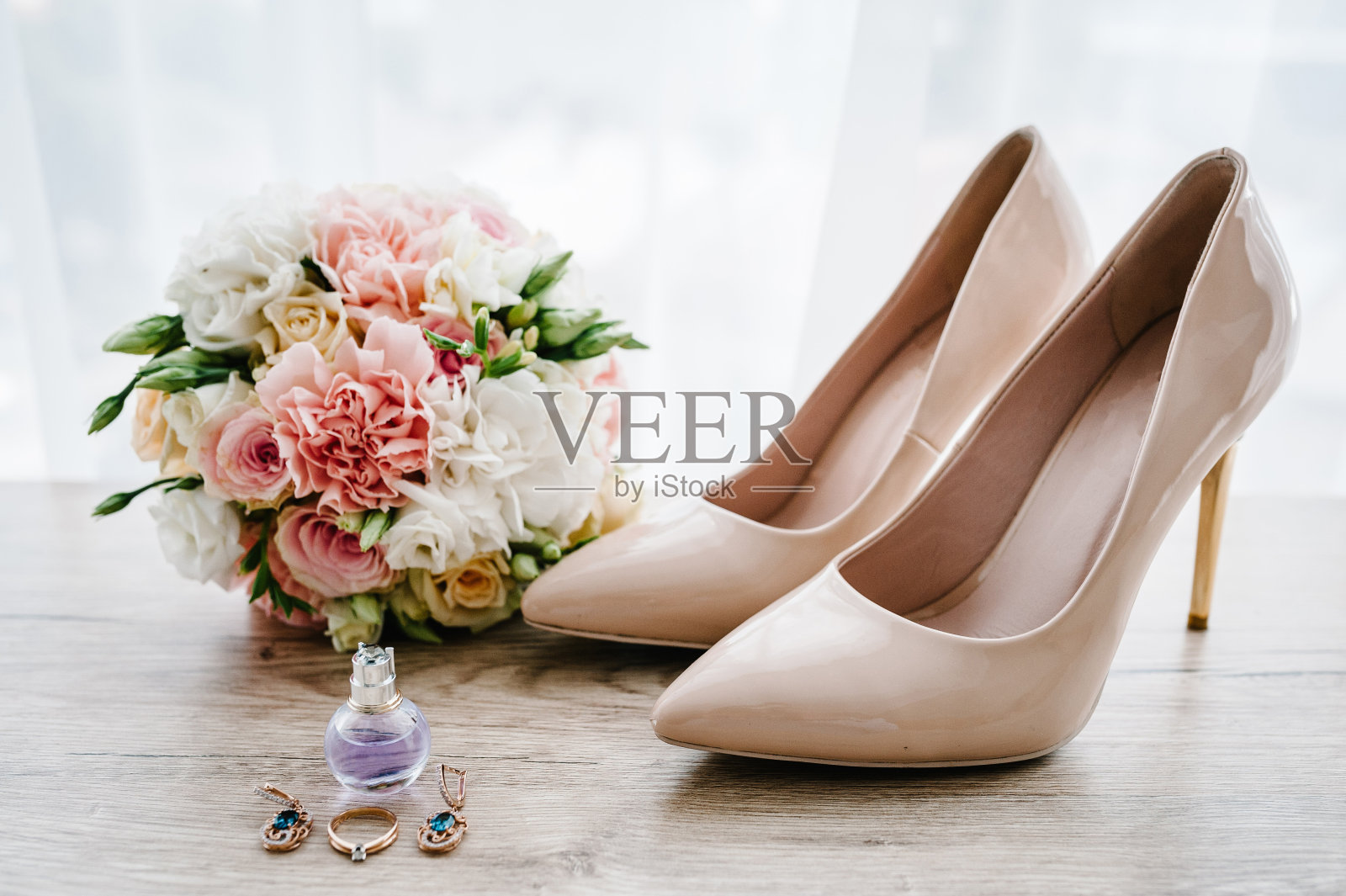 新娘的婚礼花束，粉色的玫瑰和绿色植物，时髦的经典漆米色鞋，香水，耳环和戒指躺在木制的背景。新娘配件。关闭了。侧视图。照片摄影图片