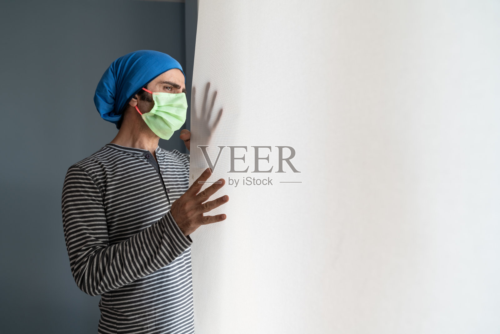 冠状病毒隔离的成年男子戴防护口罩站在窗边照片摄影图片