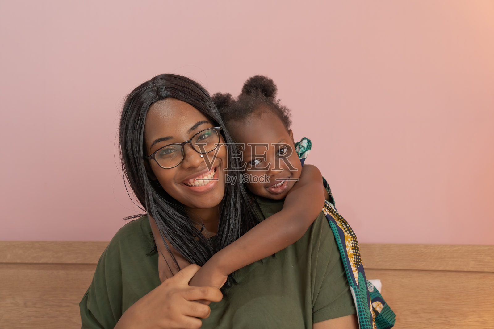 微笑的商业黑人美国妇女的肖像，一个母亲和她的女儿在家工作在家庭关系的概念在粉红色的背景。一个黑人小女孩和她的父母。照片摄影图片