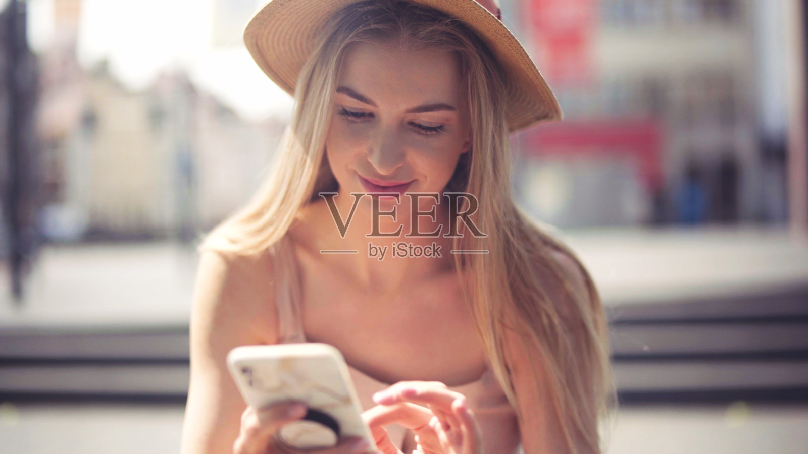 年轻的金发女人戴着帽子在城市里打电话。照片摄影图片