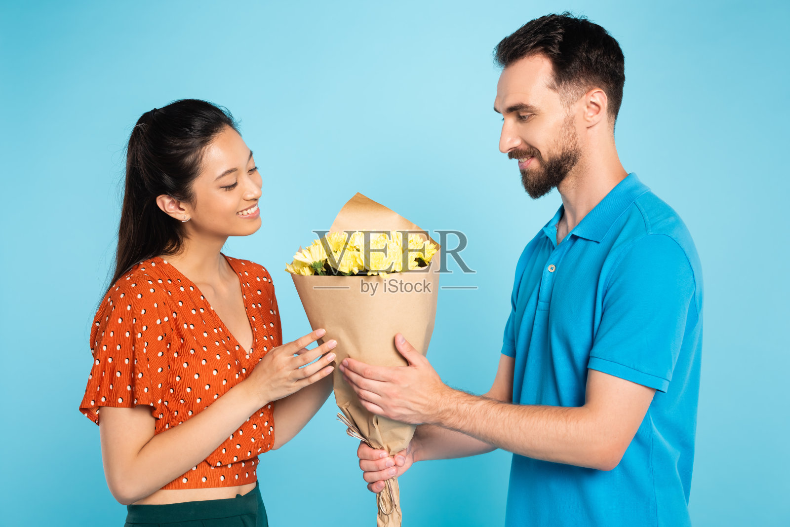 年轻男子在马球t恤献花给亚洲女友在红色衬衫上的蓝色照片摄影图片