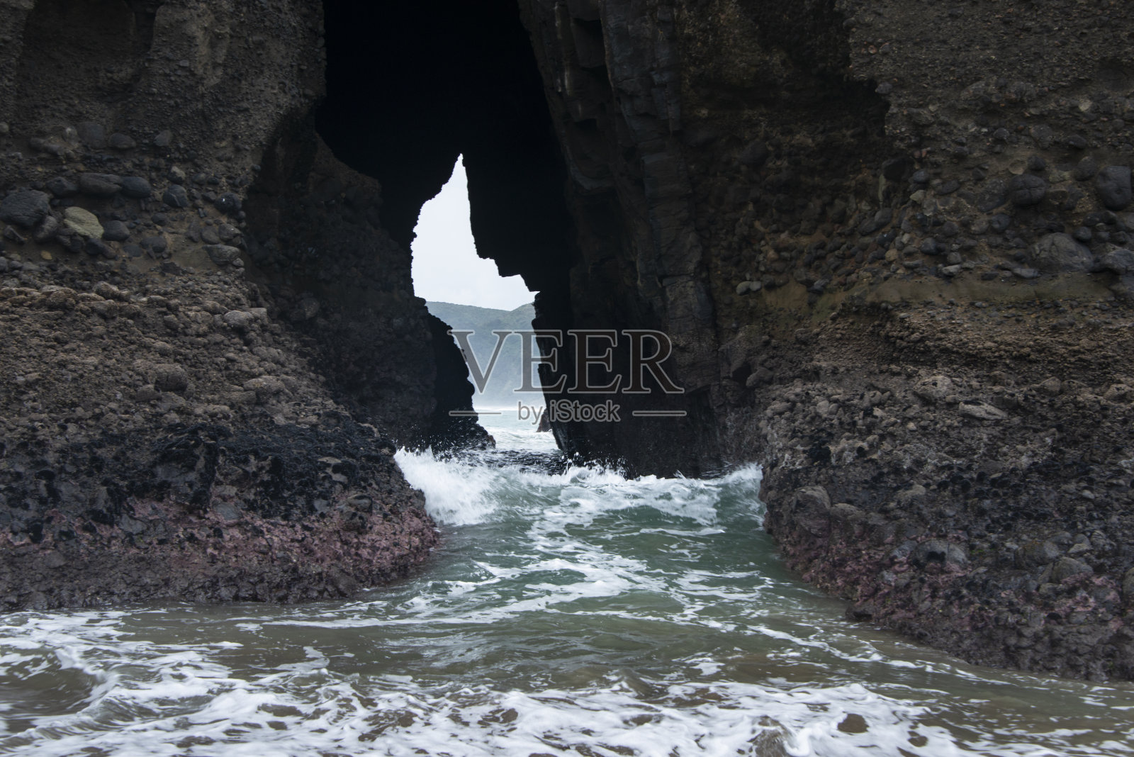 奥克兰怀塔凯尔，皮哈海滩上的锁孔岩石，海浪冲击着洞穴照片摄影图片
