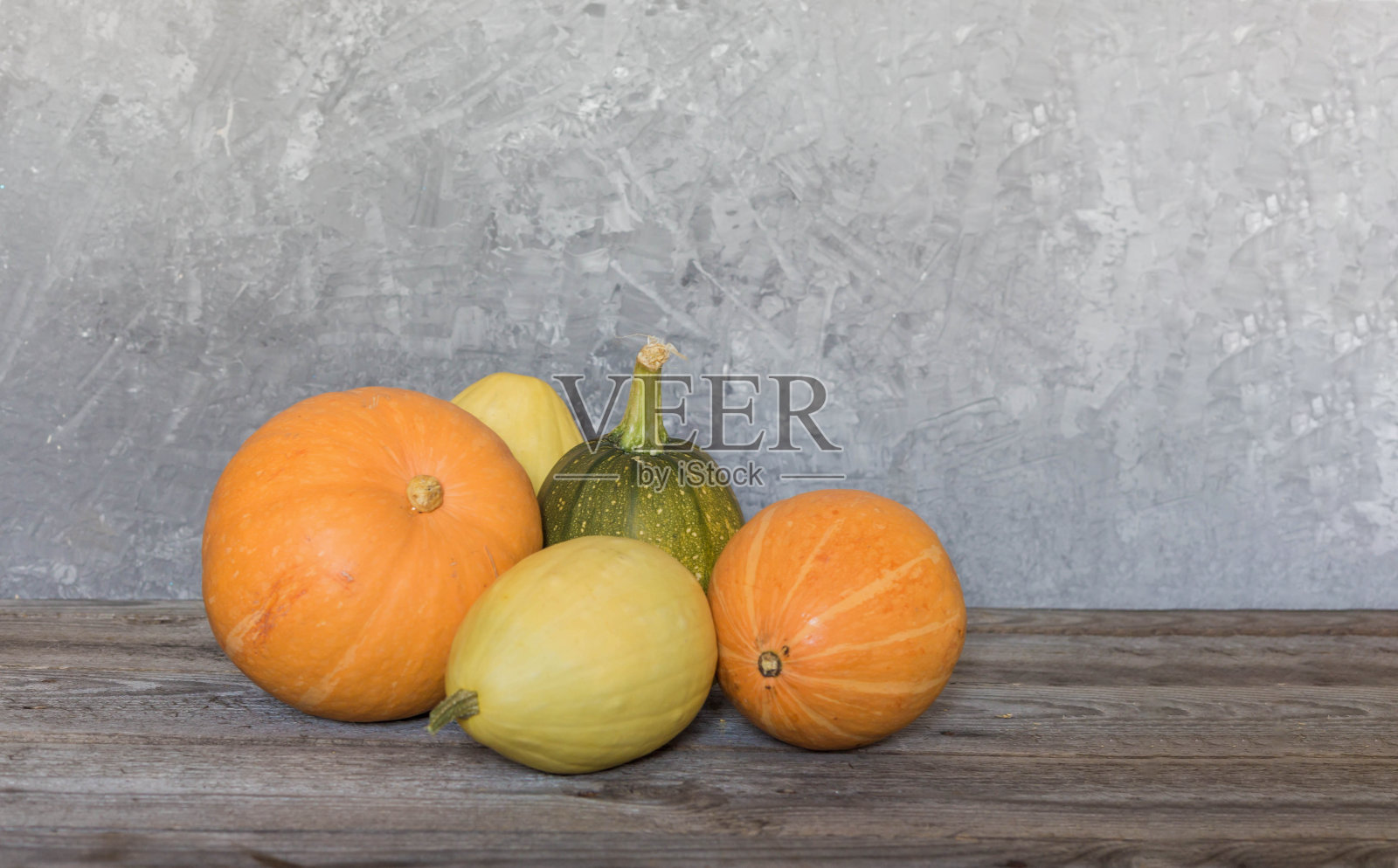 混凝土墙前的木桌上放着南瓜的秋季静物画。照片摄影图片