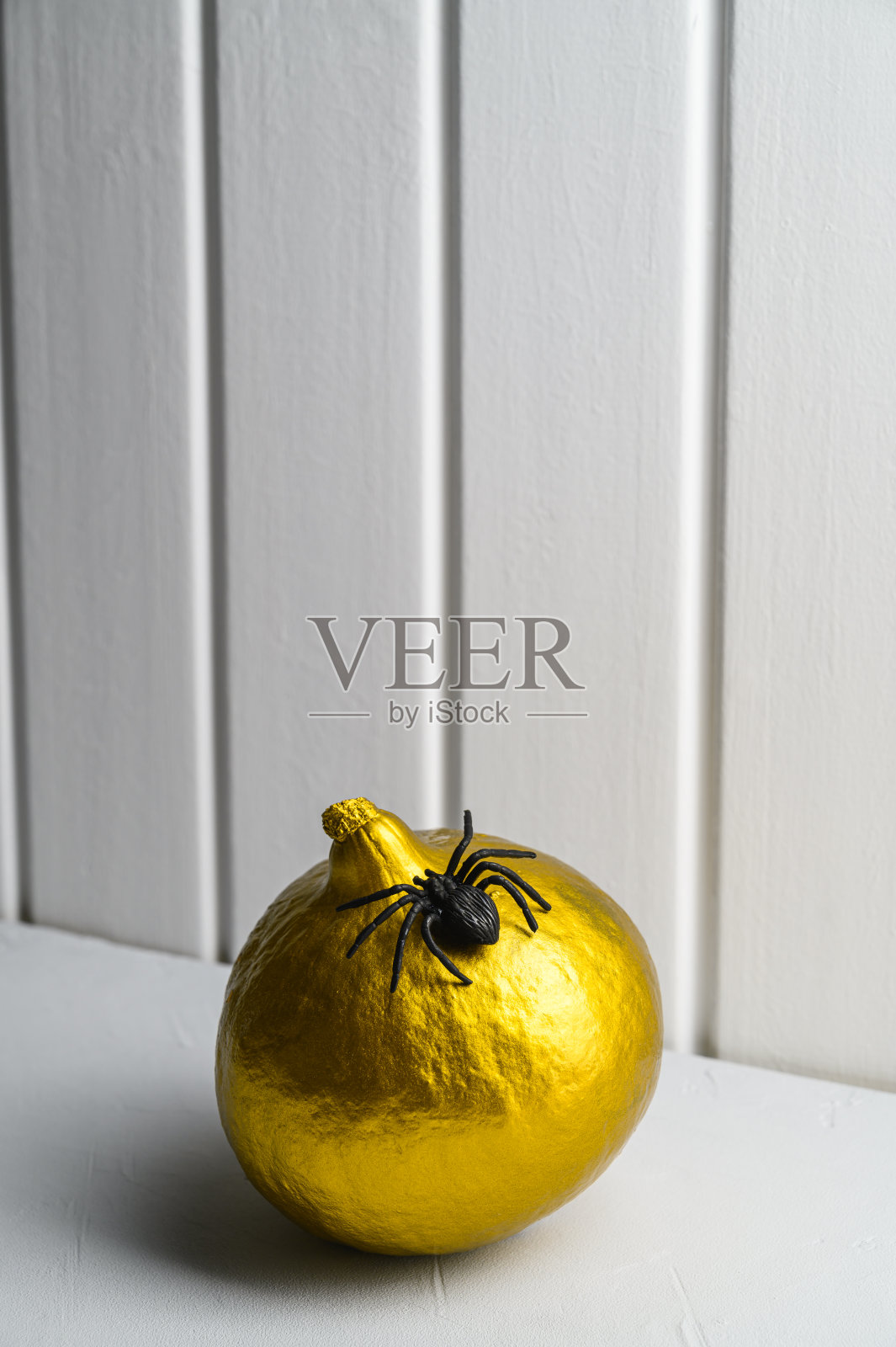 万圣节装饰品。白色木墙背景上画着一只金色的南瓜和一只蜘蛛。等距的风格。照片摄影图片