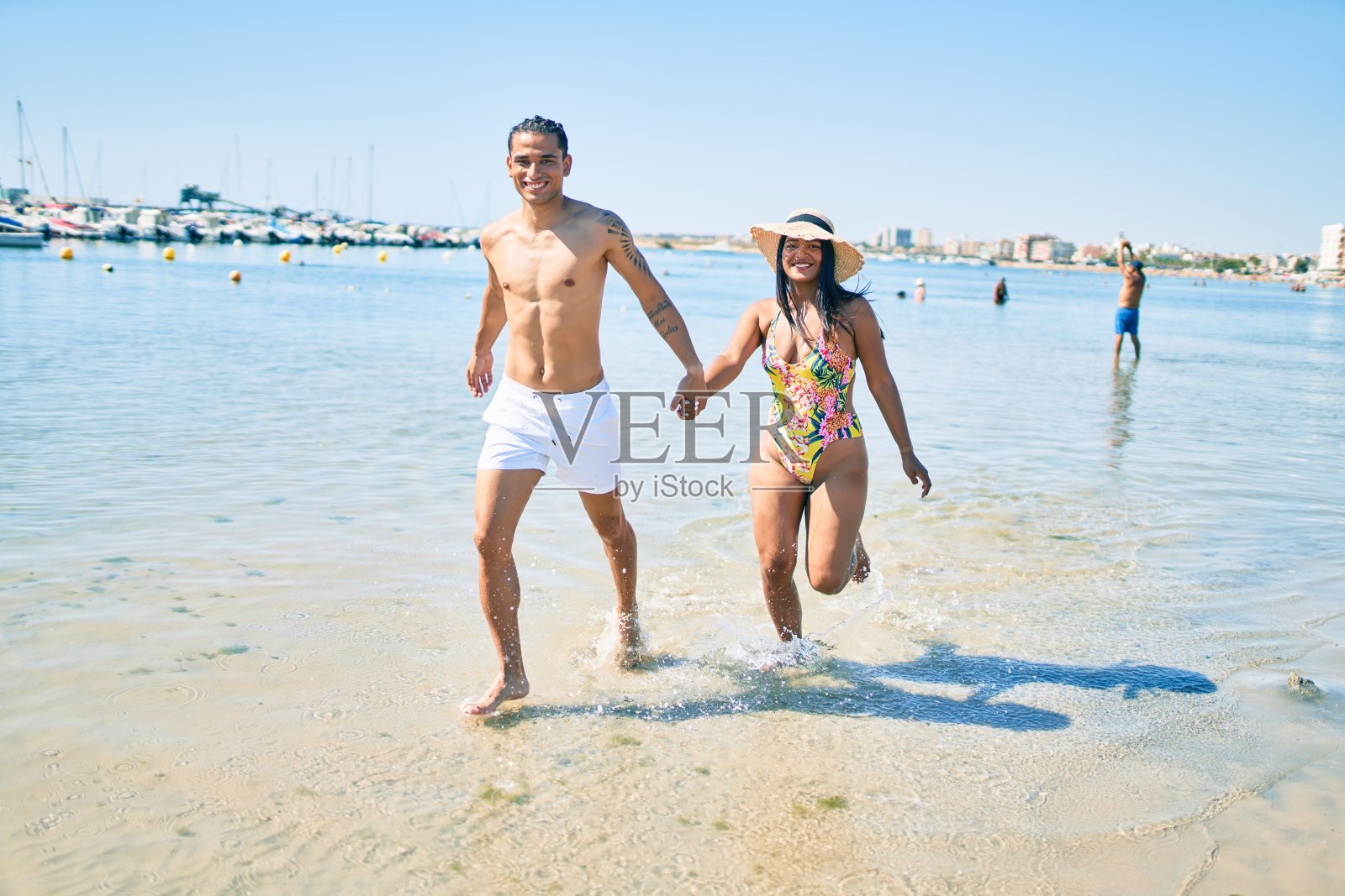 年轻的拉丁夫妇穿着泳衣在海滩上跑步。照片摄影图片