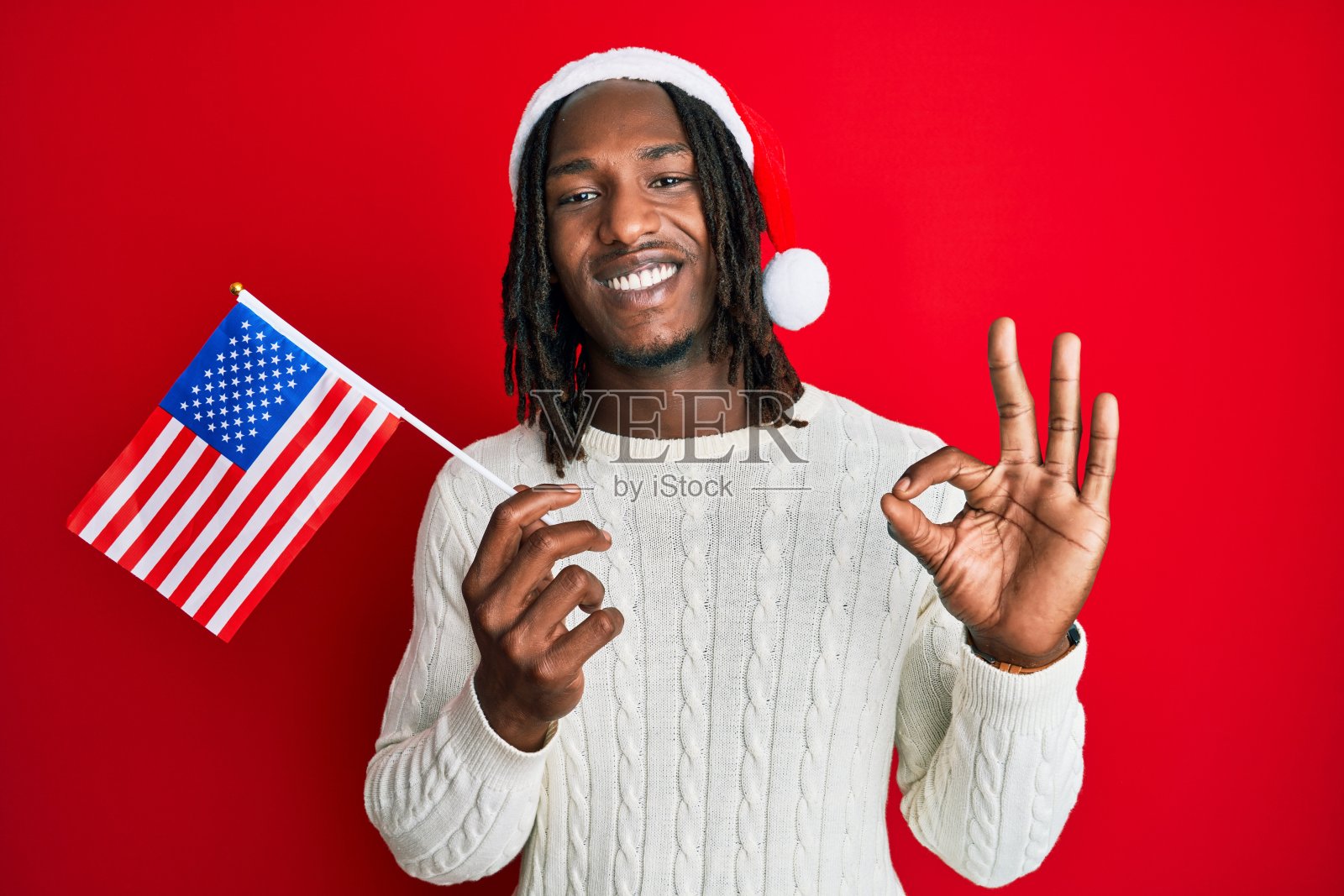 非洲裔美国人与辫子戴着圣诞帽和美国国旗做ok手势与手指，微笑友好的手势优秀的象征照片摄影图片