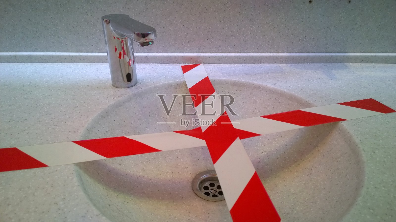 公共厕所的盥洗池和非接触水龙头，用红色胶带隔开社交距离。病毒防护的概念。卫生规则。要求。白色人造石洗手盆台面。照片摄影图片