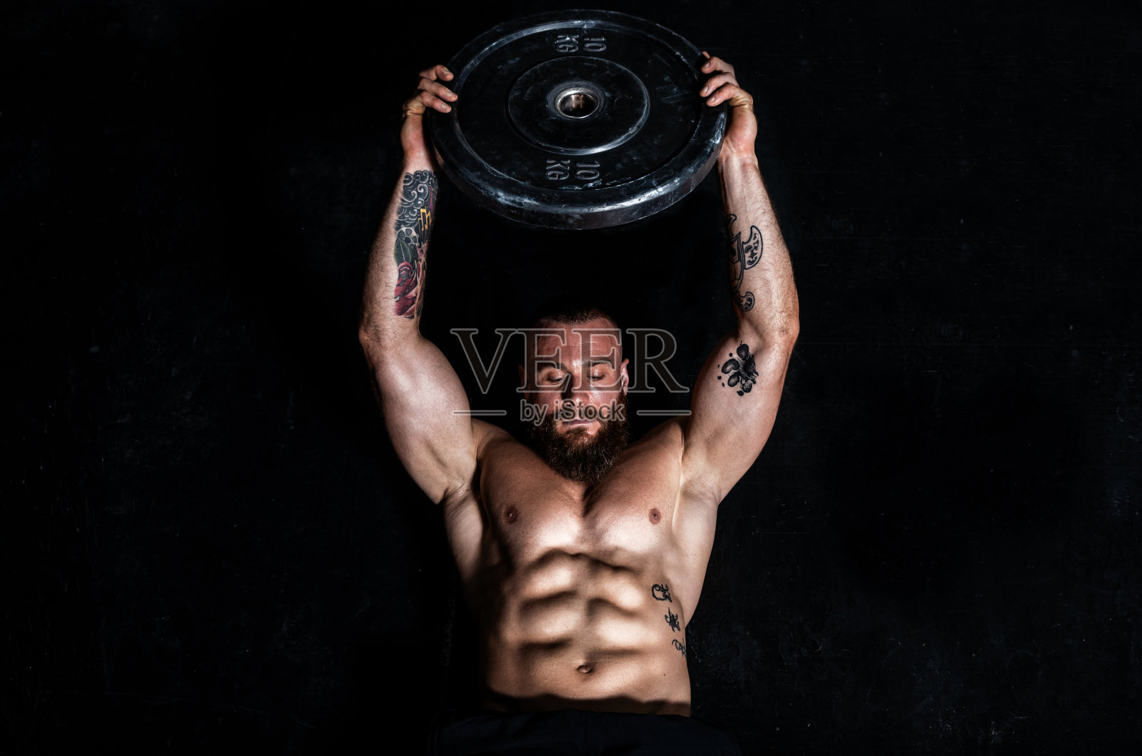 年轻的出汗适合强壮的肌肉男子与大肌肉做硬核交叉腹肌训练在健身房地板上与重量板照片摄影图片