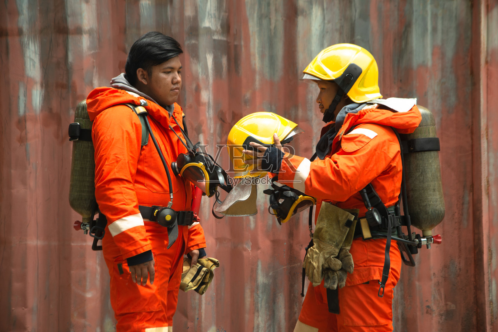 在建筑物前，身穿橙色消防制服、戴着面具和头盔的亚洲消防队员的肖像。照片摄影图片
