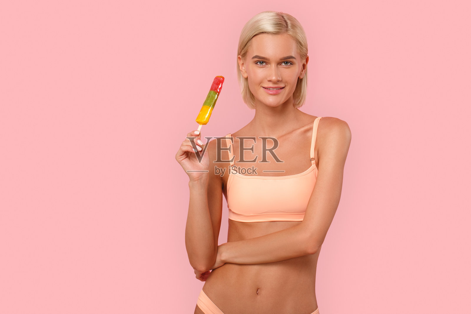 自由泳。年轻的金发女子在比基尼站在孤立的粉红色与冰淇淋摆pose相机快乐照片摄影图片