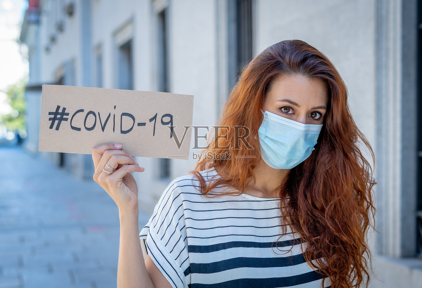 戴着医用防护口罩，举着COVID-19标牌的悲伤沮丧的女人肖像照片摄影图片