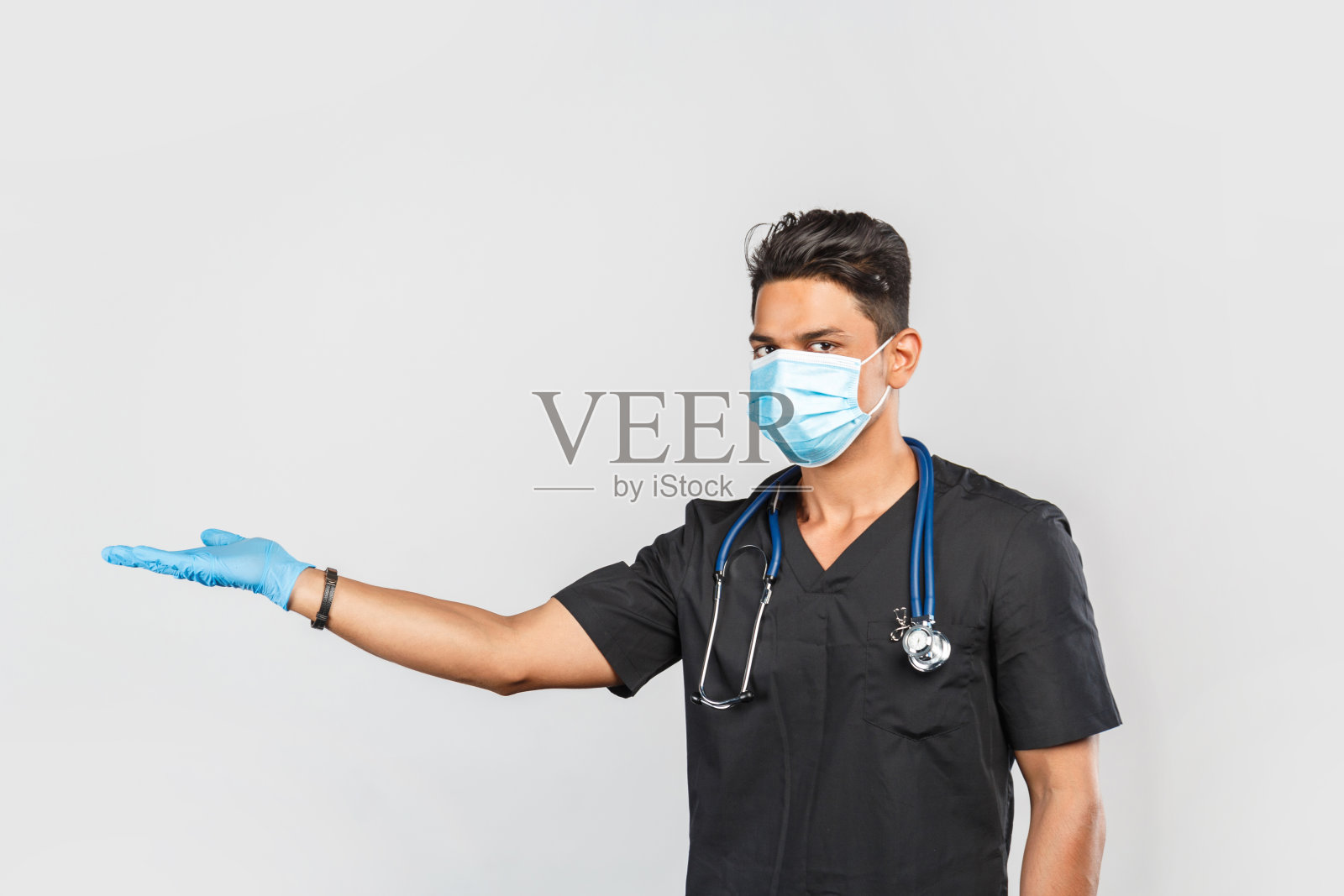 英俊的现代印度/亚洲医生戴着蓝色医用口罩和手套在灰色背景听诊器。预防冠状病毒照片摄影图片