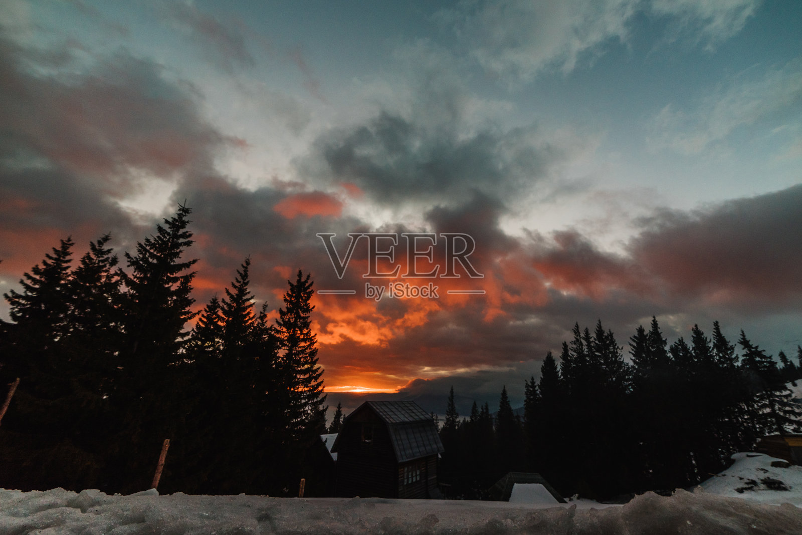 令人惊叹的红色日落与云在冬季的山脉。晚上在雪山里的房子。照片摄影图片