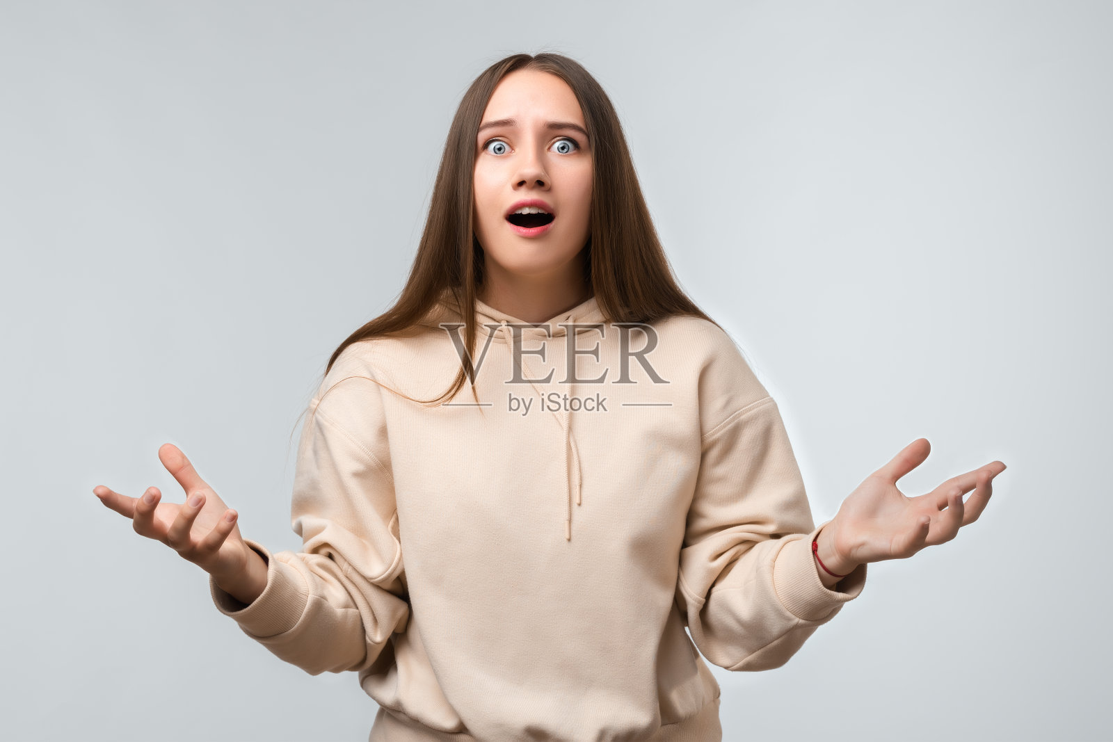 摄影棚拍摄的一名不安困惑的年轻女子，疑惑地摊开双手。怀疑、不确定和混乱的概念照片摄影图片