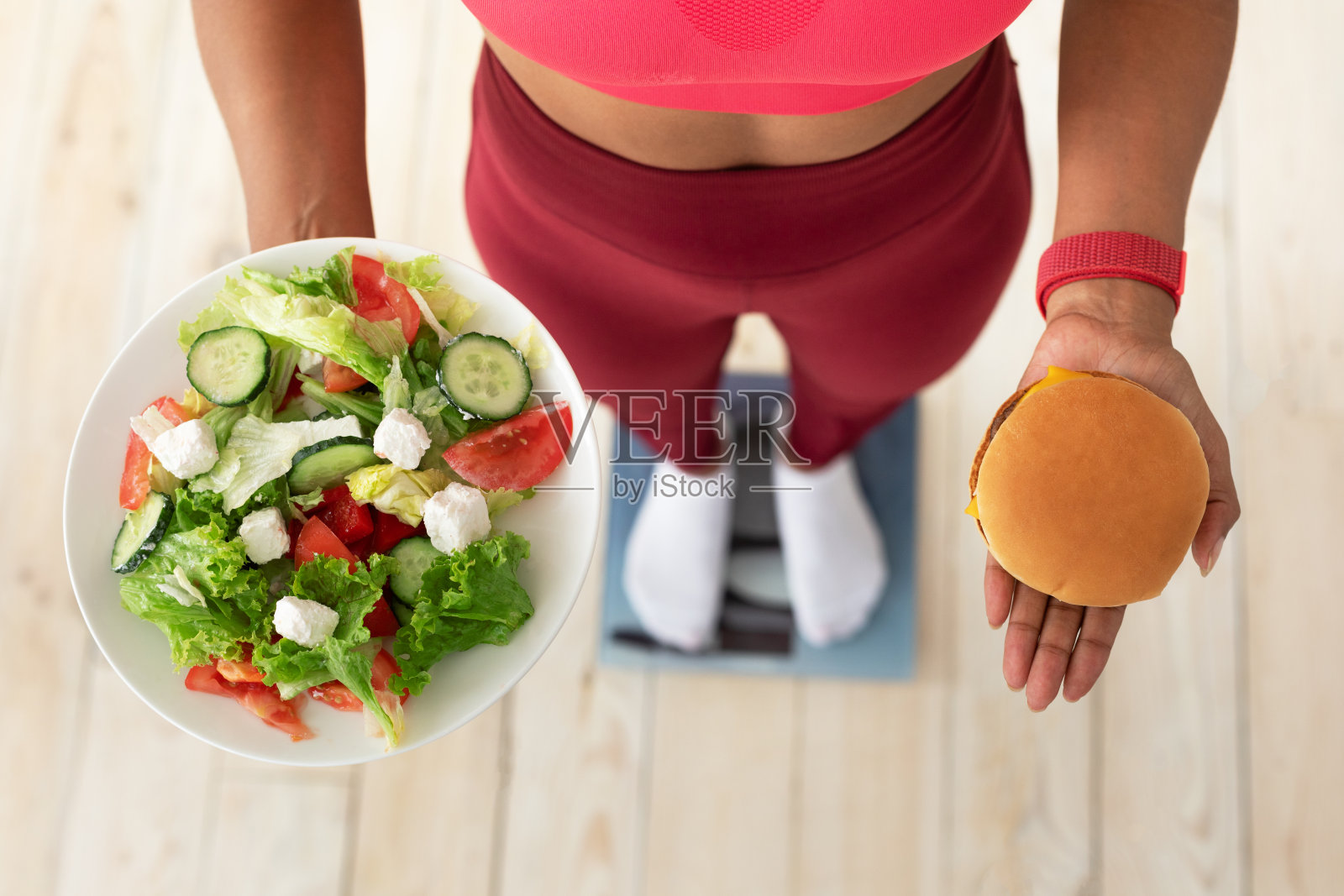 女孩站在室内秤上选择沙拉还是汉堡照片摄影图片