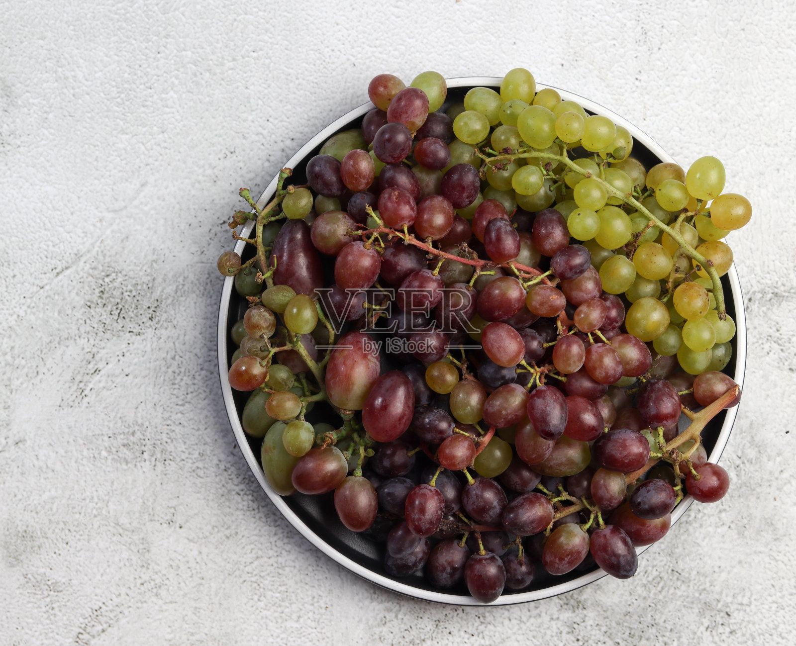 浅灰色背景的圆盘子上放着一串串成熟的葡萄照片摄影图片