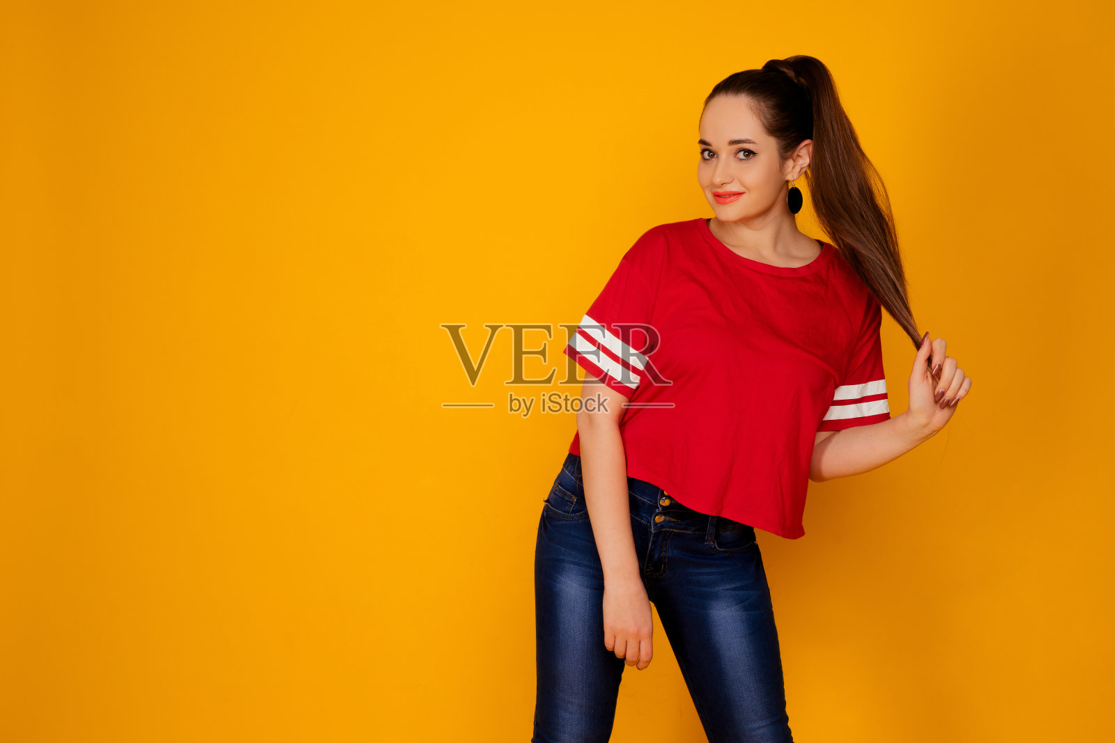 漂亮的年轻女人的肖像在时尚的红色t恤孤立在黄色的背景。她拿起她的头发。照片摄影图片
