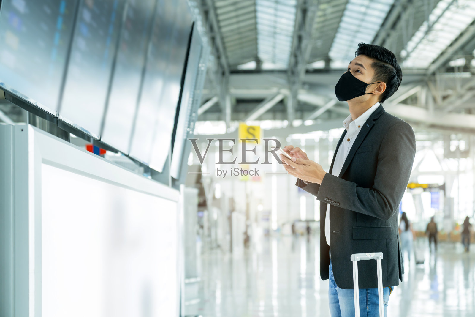 亚洲商务人士佩戴口罩，在候机楼登机信息屏幕上查看地图和航班时刻表照片摄影图片