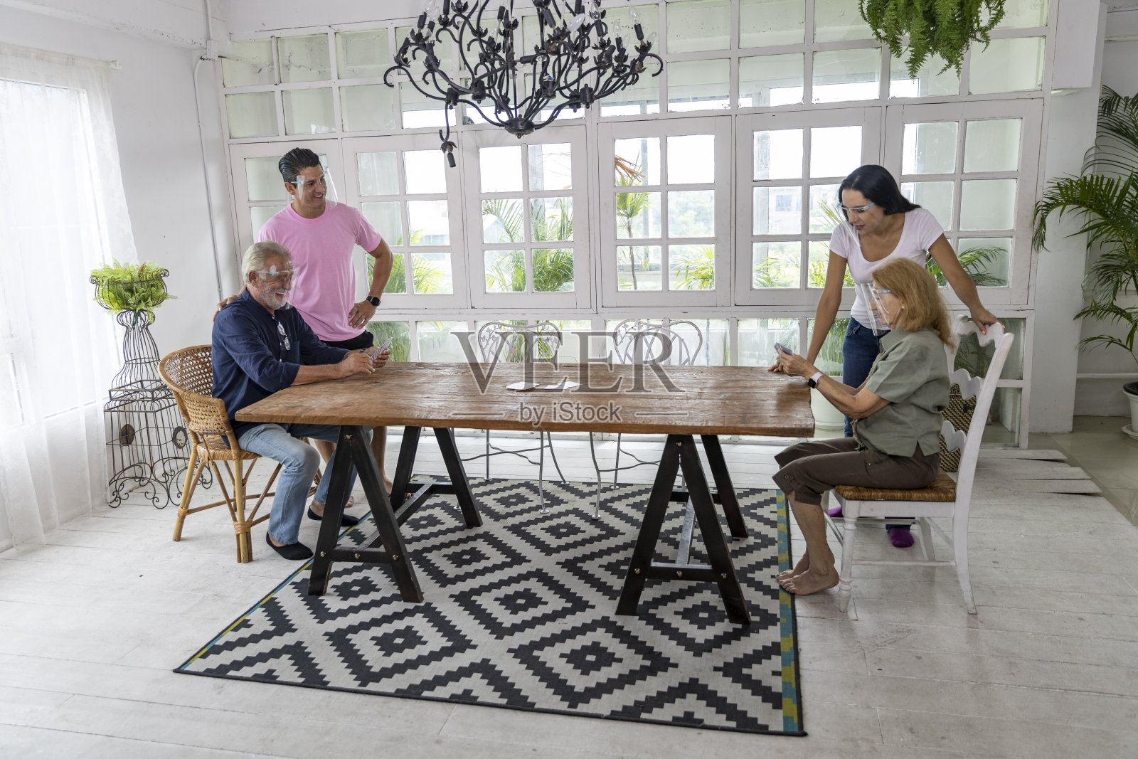 2019冠状病毒病隔离和城市封锁期间，戴面罩的家人一起打牌。家庭将居家社交距离纳入新常态，以预防冠状病毒感染照片摄影图片